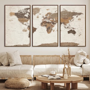 May include: Three framed world map prints in shades of brown and beige. The maps are detailed with country names and borders, set against a vintage-style background. The frames are dark brown, and the artwork is displayed above a beige sofa.