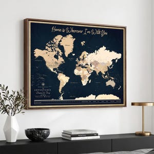May include: A rectangular wall art print featuring a world map with a dark navy blue background and light beige continents. The text reads Home is Wherever I'm With You and The Adventures of Danna & Troy. It is framed in a dark brown wood frame.