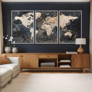 May include: Three framed world map art pieces. The maps are in a wood-grain style with a dark background and white and tan continents. The frames are white. The art is displayed above a wooden cabinet.