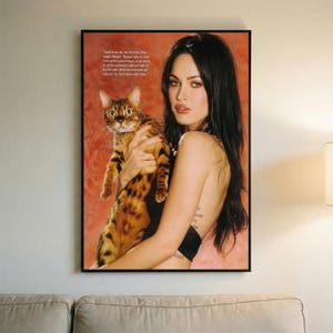 May include: A framed print featuring a woman holding a Bengal cat. The cat has a spotted coat of brown and black. The woman has long black hair and is wearing a black top. Text is visible in the upper left corner.