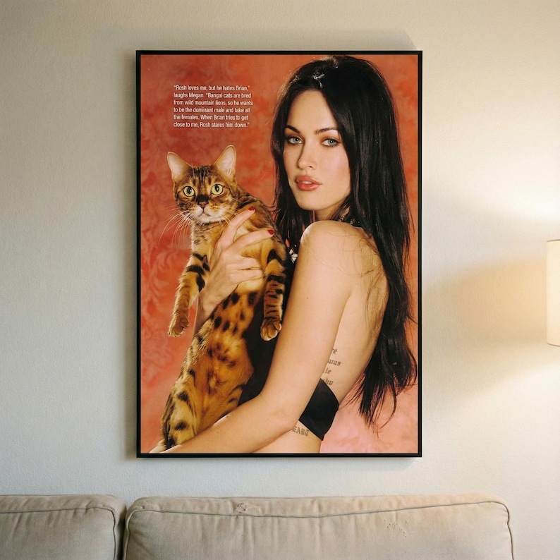 May include: A framed print featuring a woman holding a Bengal cat. The cat has a spotted coat of brown and black. The woman has long black hair and is wearing a black top. Text is visible in the upper left corner.