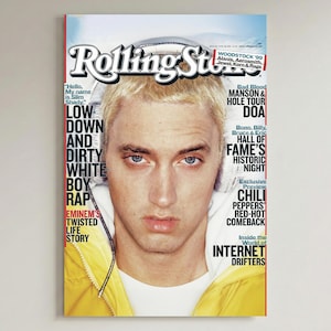 Può includere: Copertina della rivista Rolling Stone con Eminem. La copertina include il logo Rolling Stone, il testo "Woodstock '99" e altri titoli. Eminem è centrato, indossa una giacca gialla.
