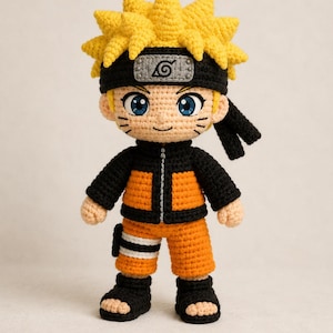 May include: A crocheted doll of a character with spiky yellow hair, wearing a black headband with a grey metal plate featuring a spiral symbol. The doll has a black and orange jacket, orange shorts, and black footwear with blue eyes and whiskers.