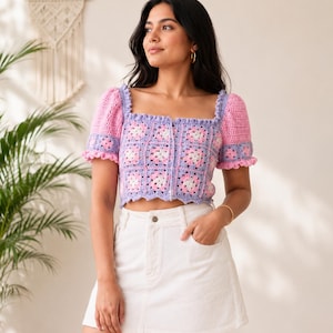 Könnte beinhalten: Kurzärmliges Häkeltop mit Patchwork-Design. Das Oberteil hat einen quadratischen Ausschnitt und Puffärmel. Das Farbschema umfasst Rosa, Lavendel und Weiß. Das Oberteil wird mit einem weißen Rock kombiniert.