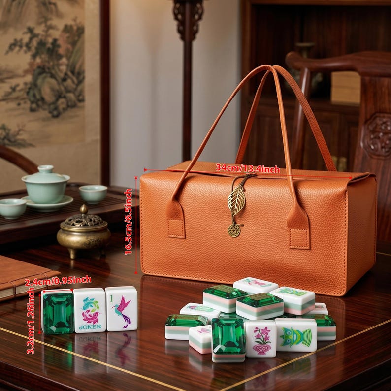 May include: An orange rectangular storage bag with two handles and a gold leaf charm, measuring 13.4 inches by 6.5 inches. Beside it are several mahjong tiles, each measuring 1.26 inches, featuring green, pink, and blue graphic designs.