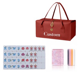 May include: A red rectangular carrying bag with the word Custom printed in white, featuring a gold leaf-shaped charm. Below are white mahjong tiles with blue letters, floral designs, and Joker icons, plus two translucent rectangular tiles.