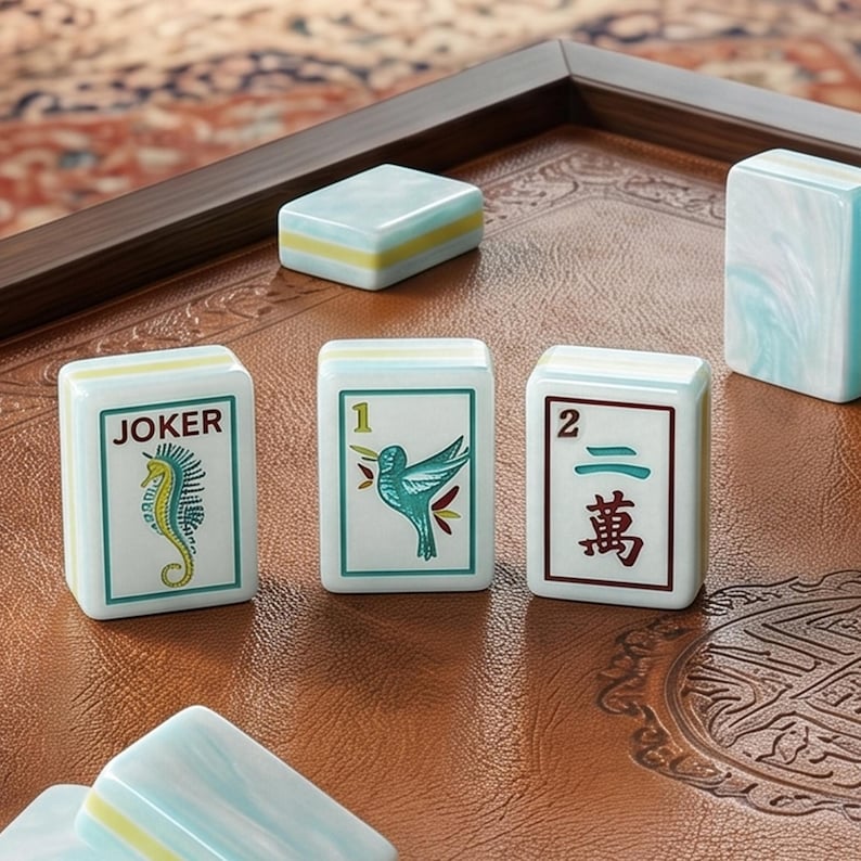 Puede incluir: Un conjunto de fichas de mahjong rectangulares con base blanca y bordes jaspeados en azul claro. Tres fichas est&aacute;n de pie, mostrando un caballito de mar con el texto JOKER, un colibr&iacute; con el n&uacute;mero 1 y el n&uacute;mero 2 con caracteres chinos.