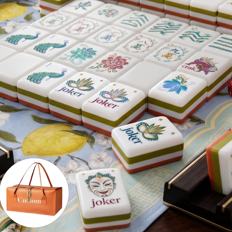 May include: A set of white mahjong tiles with green and orange bases, featuring colorful illustrations of peacocks, flowers, and masks. Several tiles are labeled with the word joker. An inset shows a tan rectangular carrying bag with the word Custom.