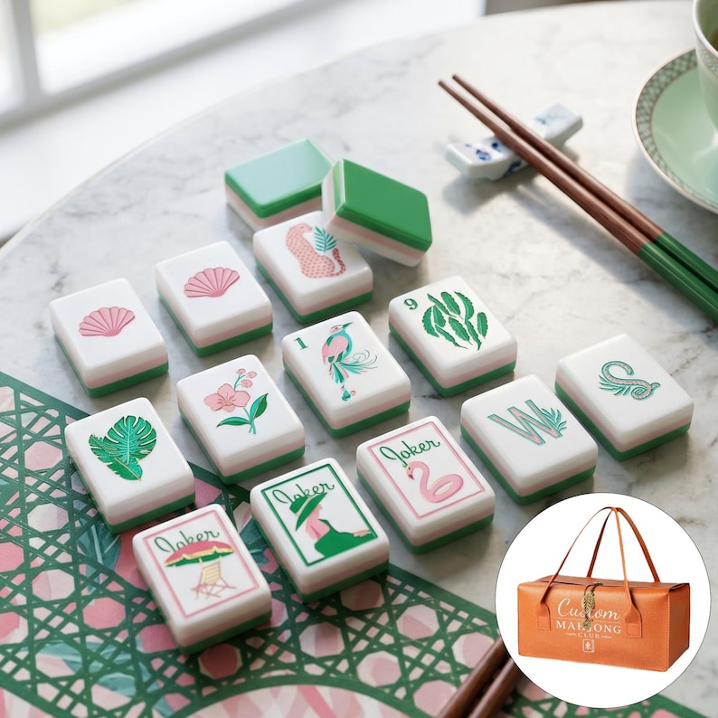 May include: A set of rectangular Mahjong tiles with white faces and green backs, featuring colorful illustrations of shells, flowers, birds, leaves, and the word Joker. A brown carrying bag with the text Custom Mahjong Club is also included.