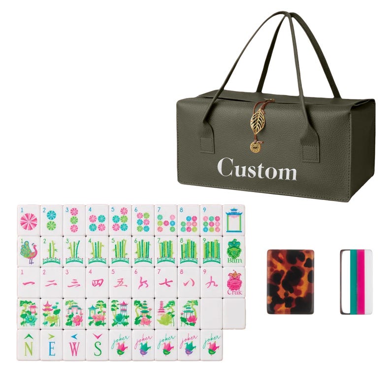 May include: An olive green rectangular carrying bag with the word Custom printed in white, featuring a gold leaf charm. A set of white mahjong tiles with colorful floral, bamboo, and character designs, plus two additional tiles with tortoise shell and striped patterns.