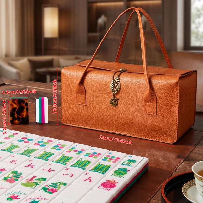 May include: A rectangular orange textured carrying case with two handles and a leaf-shaped metal charm closure. The case measures 13.4 inches long and 6.5 inches high. Beside it are mahjong tiles, including one measuring 1.26 inches by 0.95 inches.