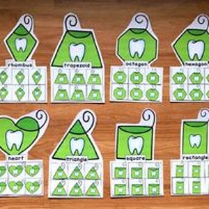 Może przedstawiać: Zestaw edukacyjnych kart kształtów o tematyce dentystycznej. Każda karta przedstawia inny kształt, taki jak gwiazda, romb i koło, z grafiką zęba i przykładami kształtów. Karty są zielone i białe.