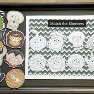May include: A Halloween matching game with monster cutouts and a card featuring a green, purple, and white chevron pattern. The card reads "Match the Monsters" in a black rectangle. The game is on a dark grey tray.