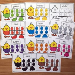 Peut inclure: Ensemble de cartes éducatives avec des poussins et des œufs de dessins animés colorés. Chaque carte présente une couleur différente, comme le vert, le jaune et le rouge, avec des œufs correspondants et le nom de la couleur imprimé. Les cartes sont conçues pour l'apprentissage et la reconnaissance des couleurs.