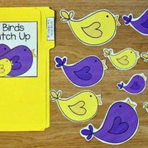 May include: A yellow file folder with the text "Spring Birds Size Match Up" and several cut-out bird shapes in yellow and purple. The birds vary in size and are arranged on a wooden surface.