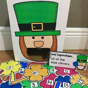 Può includere: Un colorato gioco a tema San Patrizio con una faccia da folletto e una fessura per l'alimentazione. Include ritagli di trifogli numerati in vari colori e un cartello che recita "Feed Leprechaun... all of the blue clovers."