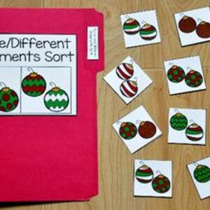 May include: A red file folder with a white label that reads "Same/Different Ornaments Sort." Several square cards with Christmas ornament illustrations are scattered on a wooden surface. The ornaments are red, green, and white.