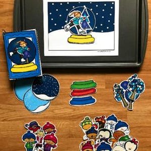 Puede incluir: Una colección de manualidades de papel troquelado y colorido con temática invernal. El conjunto incluye una ilustración de globo de nieve, varias figuras de invierno y elementos decorativos como árboles y nieve. Los artículos están dispuestos sobre una superficie de madera y una bandeja gris oscuro.