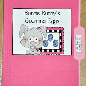 以下が含まれることがあります： 「Bonnie Bunny's Counting Eggs」と書かれたラベルが付いたピンク色のファイルフォルダー。ラベルには漫画のウサギと3つの装飾されたイースターエッグが描かれています。右側のタブにも同じテキストがあります。