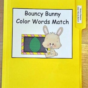 Puede incluir: Una carpeta amarilla etiquetada como "Bouncy Bunny Color Words Match". La carpeta presenta un conejito de dibujos animados sosteniendo un crayón junto a una pizarra con un huevo verde. La carpeta es para fines educativos.