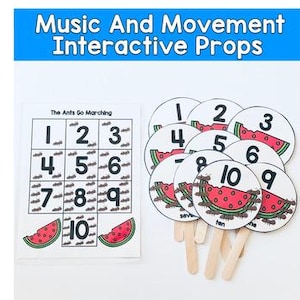Op de afbeelding: Een set interactieve muziek- en bewegingsrekwisieten voor kinderen. Bevat een kaart met cijfers en mieren, en ronde rekwisieten met watermeloen-thema met de cijfers 1-10. De tekst "Music And Movement Interactive Props" staat bovenaan.