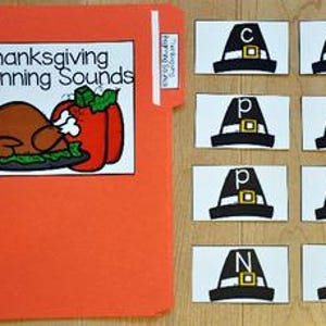 Può includere: Una cartella arancione con l'etichetta "Thanksgiving Beginning Sounds" con un'illustrazione di tacchino e peperone. Accanto, carte con grafici di cappelli da pellegrino e lettere: C, M, P, P, P, T, N e C. Materiale didattico.