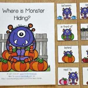 May include: A spiral-bound children's book titled "Where is Monster Hiding?" with a purple monster illustration. Accompanying cards show the monster in various positions relative to objects, such as "between" and "on top of."