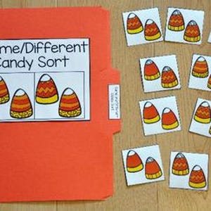 以下が含まれることがあります： 「Same/Different Candy Sort」と書かれた白いラベルが付いたオレンジ色のファイルフォルダー。ラベルには、キャンディーコーンの画像が表示されています。いくつかのキャンディーコーンカードが木製の表面に散らばっています。