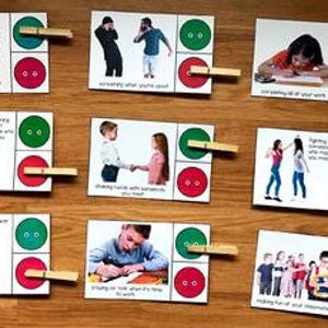 Può includere: Una serie di schede didattiche con immagini e testo, ciascuna raffigurante una diversa situazione sociale. Le schede hanno bottoni verdi e rossi e sono fissate con mollette di legno. Disposte su una superficie di legno.