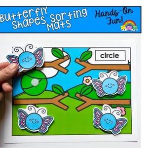 May include: A colorful educational game featuring butterfly shapes and sorting mats. The image shows a hand placing a butterfly shape onto a matching circle on a mat. The mat has a blue sky, green grass, and tree branches. Text on the mat reads "Butterfly Shapes Sorting Mats".