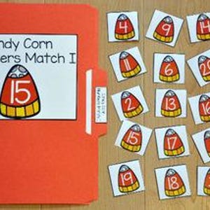 Puede incluir: Una carpeta naranja con una etiqueta blanca que dice "Candy Corn Numbers Match I" y el número 15. Al lado hay 20 tarjetas en forma de caramelos de maíz, cada una con un número diferente del 1 al 20.