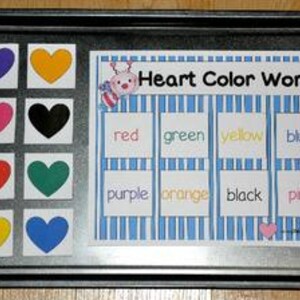 May include: A baking tray displays a colourful educational chart. Nine heart-shaped cutouts in various colours are on the left. A card on the right reads "Heart Color Words" with colour names: red, green, yellow, blue, purple, orange, black, and pink.