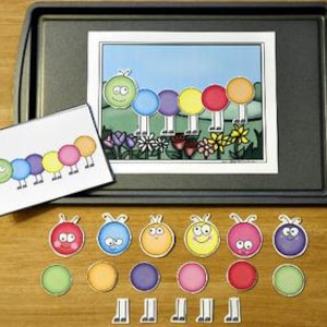 Può includere: Un colorato set di attività educative a tema bruco. Include un'illustrazione stampata di un bruco in un giardino, una scheda abbinata e singole parti del corpo e zampe del bruco. Il set è disposto su un vassoio grigio scuro.