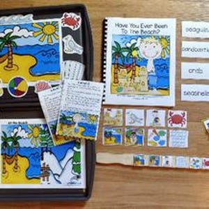 May include: A children's educational beach-themed set with illustrations and text. Includes a book titled "Have You Ever Been To The Beach?" and various picture cards, along with magnetic pieces and labels like "sand" and "sun".