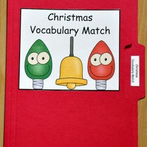 May include: A red file folder with a white label featuring the text "Christmas Vocabulary Match." The label includes illustrations of a green lightbulb, a yellow bell, and a red lightbulb, all with smiling faces.