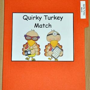 以下が含まれることがあります： オレンジ色のファイルフォルダー。白い長方形に「Quirky Turkey Match」の文字と、2羽の漫画の七面鳥のイラストが描かれています。1羽はメガネをかけカメラを持ち、もう1羽は医者のマスクをしてクリップボードを持っています。タブの小さなラベルには「Quirky Turkey Match」と書かれています。