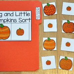 May include: An orange file folder with the text "Big and Little Pumpkins Sort" and several small cards with orange pumpkin illustrations. The pumpkins vary in size and design, with green stems. The folder is on a wooden surface.