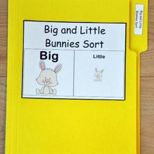 Può includere: Una cartella gialla con l'etichetta "Big and Little Bunnies Sort". La cartella ha un'etichetta bianca con il titolo e le illustrazioni di un coniglio grande e piccolo. La cartella è su una superficie di legno.