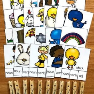 Peut inclure: Ensemble de cartes éducatives illustrées avec des dessins colorés, dont un soleil, un cerf-volant et un arc-en-ciel. Les cartes sont disposées sur une surface en bois, avec des pinces à linge en dessous.