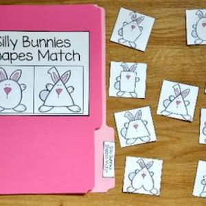May include: A pink file folder with the text "Silly Bunnies Shapes Match" on a white label. Several small square cards with bunny illustrations are scattered on a wooden surface, each with a different shape.