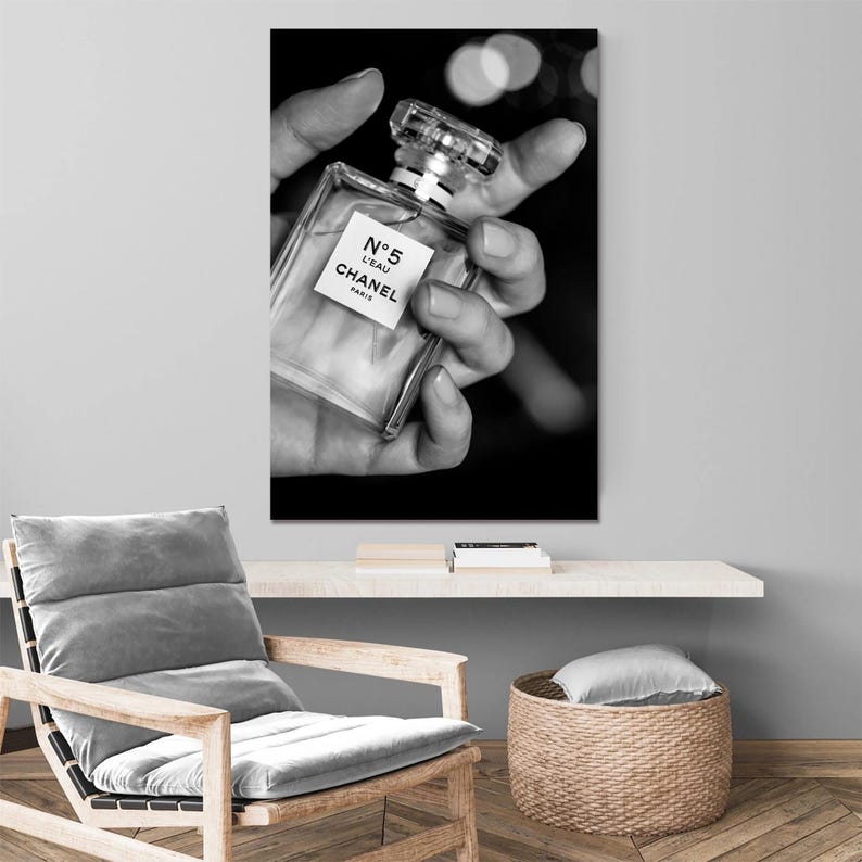 Puede incluir: Una impresi&oacute;n de arte mural en blanco y negro que muestra un frasco de perfume rectangular de vidrio con un tap&oacute;n transparente. La etiqueta del frasco muestra claramente el texto N&deg;5 L'EAU CHANEL PARIS. El frasco se sostiene en una mano.