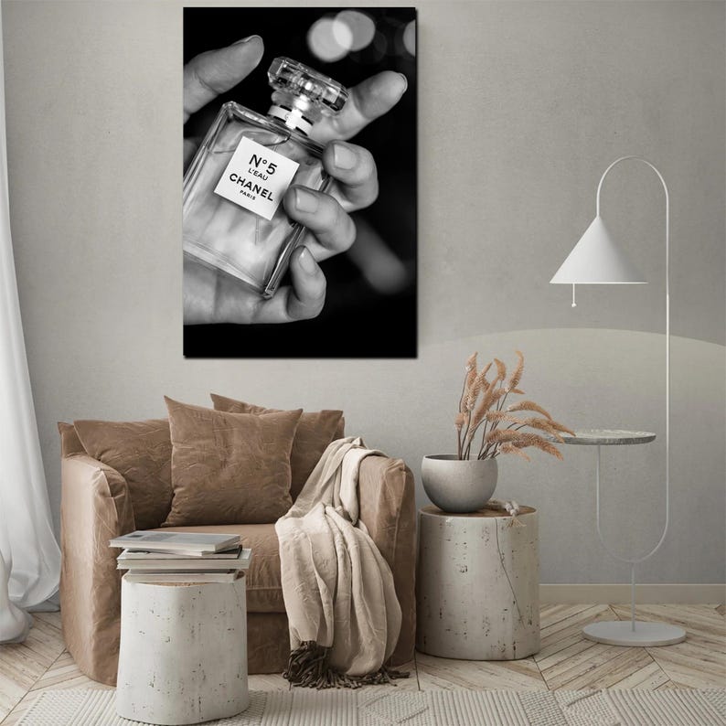 Puede incluir: Una impresi&oacute;n de arte mural en blanco y negro que muestra un frasco de perfume rectangular de vidrio con un tap&oacute;n transparente. La etiqueta del frasco muestra claramente el texto N&deg;5 L'EAU CHANEL PARIS. El frasco se sostiene en una mano.