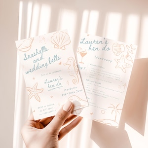 Pode incluir: Dois cartões de convite creme com tema de praia. O cartão esquerdo diz "Seashells and wedding bells" e "Lauren's hen do". O cartão direito é um itinerário. Ambos os cartões têm ilustrações de conchas e cavalos-marinhos.