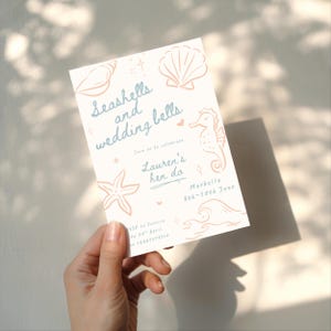 Peut inclure: Une invitation cr&egrave;me avec le texte "Seashells and wedding bells" et des illustrations de coquillages, d'un hippocampe et d'une &eacute;toile de mer. L'invitation est pour l'enterrement de vie de jeune fille de Lauren &agrave; Marbella du 8 au 10 juin.