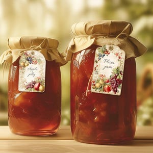 Peut inclure: Deux bocaux en verre remplis de confiture rouge foncé, chacun surmonté d'un couvercle en papier beige attaché avec de la ficelle. Le petit bocal porte une étiquette Apple jelly et le grand une étiquette Plum jam, ornées d'illustrations de fruits.
