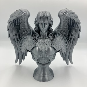 May include: A gray bust of an angel with large, detailed wings. The angel has long, flowing hair and wears ornate armor. The sculpture is mounted on a pedestal base, and the overall design is highly detailed.