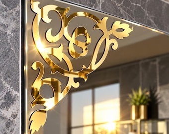 May include: A gold-colored, reflective corner decal featuring an intricate, symmetrical scrollwork pattern with leaf-like motifs. The decorative piece is applied to the upper corner of a rectangular mirror, creating a polished, metallic finish.