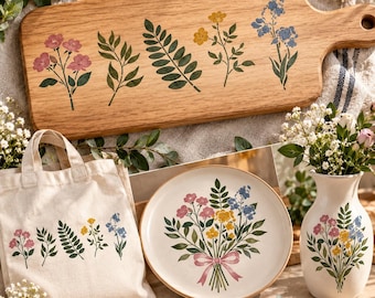 May include: A wooden cutting board, a canvas tote bag, a ceramic plate, and a ceramic vase, all featuring matching botanical illustrations of pink, yellow, and blue flowers with green leaves and stems, with a pink ribbon on the plate.