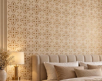 May include: A bedroom wall featuring a repeating floral quatrefoil pattern in metallic gold on a cream background. The wall is positioned behind a beige upholstered headboard with vertical channel tufting and layered neutral-toned bedding.