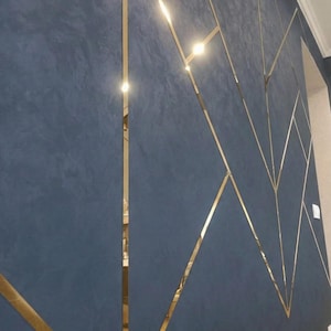 May include: A wall surface featuring a deep blue, textured finish with a matte appearance. The wall is divided by thin, reflective gold-colored metal strips arranged in a geometric pattern of intersecting lines and angular shapes.
